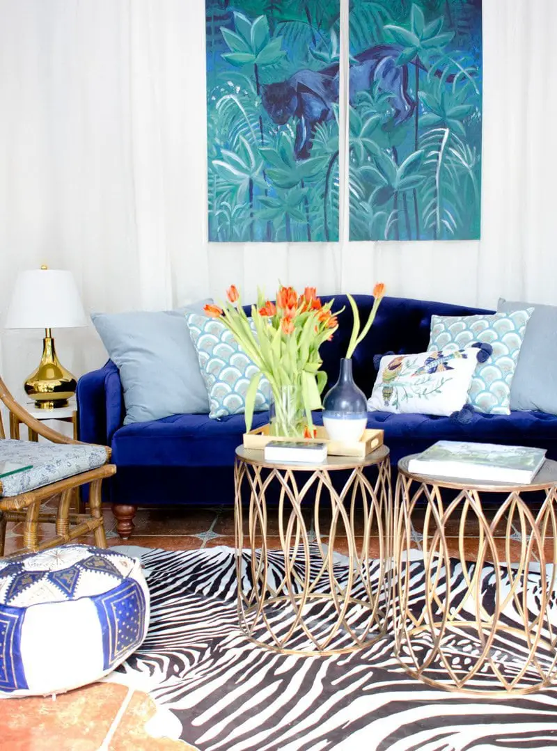 Eclectic living room with blue velvet sofa, zebra rug, and bronze bunching tables.