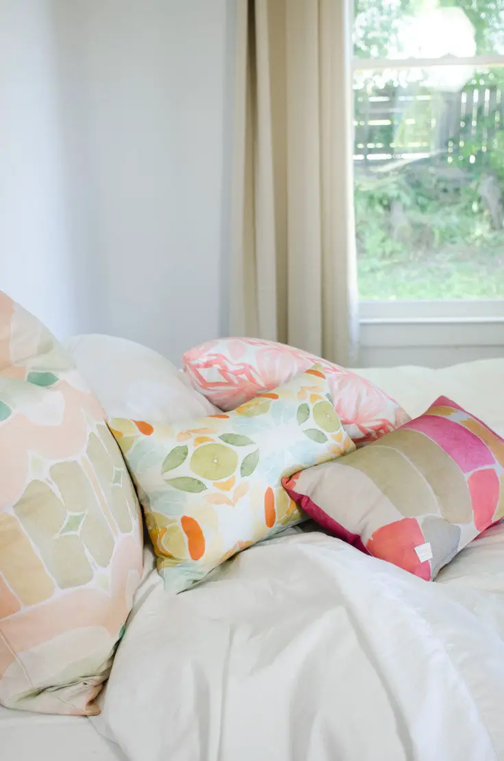 White bedroom with splashes of colorful watercolor patterns from bunglo's pillow collection.