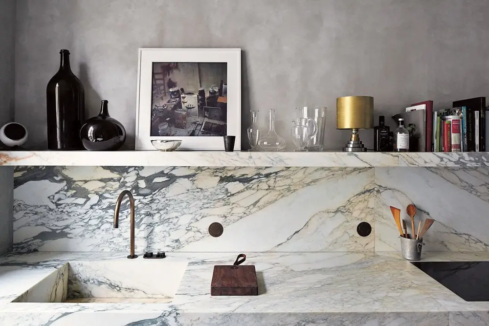 Sleek veined marble and a floating shelf above the kitchen sink.