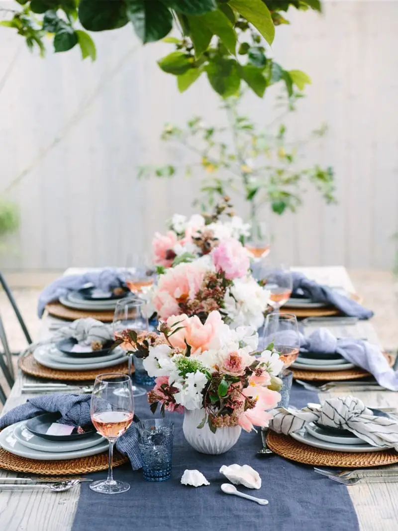 Summer outdoor dining table setting with blue napkins and pink flower arrangements on Thou Swell @thouswellblog