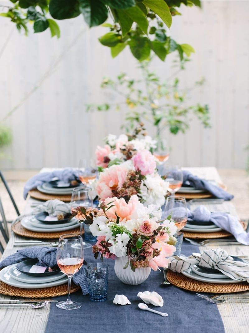 Summer outdoor dining table setting with blue napkins and pink flower arrangements on Thou Swell @thouswellblog