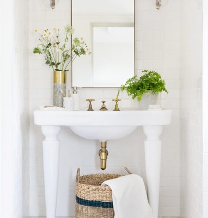 Classic white bathroom with subway tile, fern, glass sconces, and wicker basket storage on Thou Swell @thouswellblog #bathroom #bathroomdesign #classicbathroom #classicdesign #interiordesign