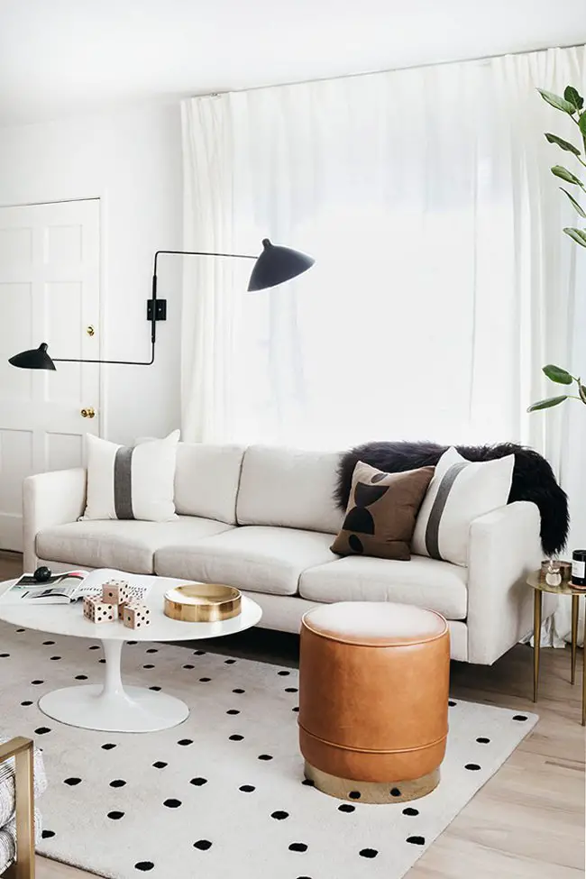 Modern living room with white sofa, leather stool, Saarinen marble coffee table, spotted rug, and black two-arm sconce on Thou Swell @thouswellblog #livingroom #moderndesign #modernroom #moderninterior #interiordesign #whitesofa #modernlivingroom