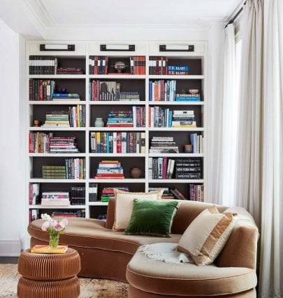 A cozy living room corner with built-in bookshelves, curvy velvet sofa, traditional rug, and wicker side table on Thou Swell #livingroom #livingroomdesign #traditionaldesign #transitionaldesign #neotraditional #interiordesign #homedecor #homedecorideas #shelfie #curvedsofa