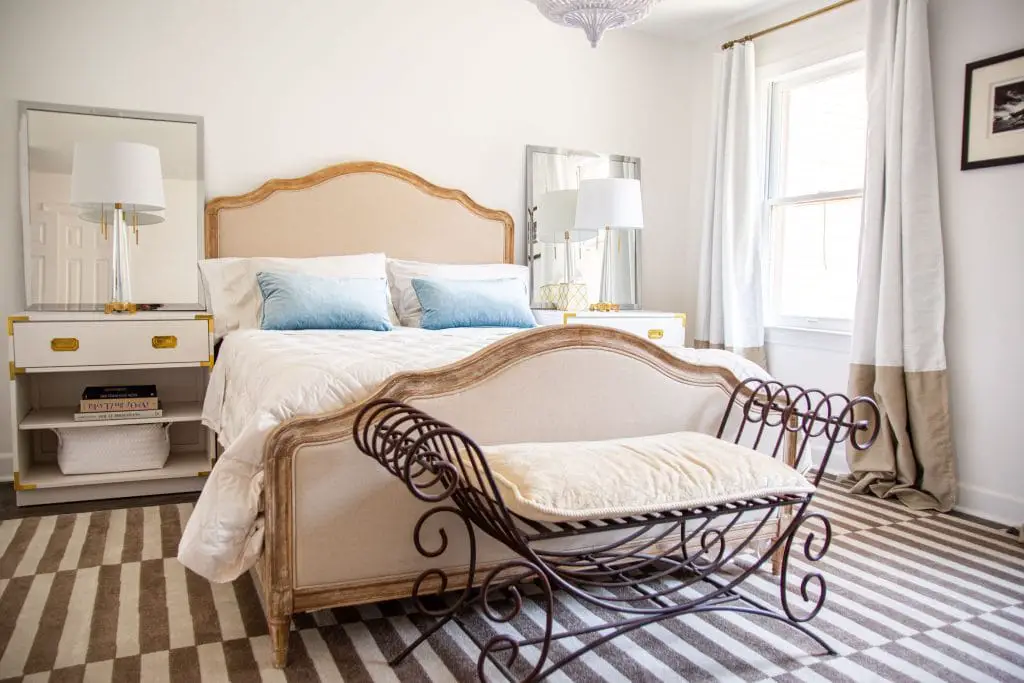 Master bedroom design with french-style upholstered bed, iron bench, and campaign nightstands in white with striped rug by Kevin O'Gara on Thou Swell #bedroom #masterbedroom #bedroomdesign #bedroomdecor #masterbedroomdesign #neutralbedroom #luxurybedroom #interiordesign #homedesign #homedecor