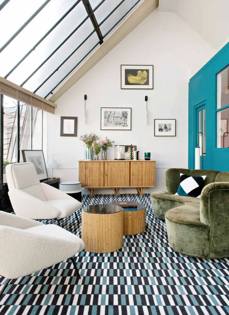 Get the look: colorful loft living room in Paris, France with green curved sofa, teal accent wall, patterned carpet, skylights, and a window wall on Thou Swell #livingroom #paris #colorful #colorfuldesign #livingroomdesign #parisloft #parisapartment #parisstyle #frenchstyle #frenchinterior #parishome #frenchhome #parisian #parisianstyle #loftdesign #homedecor