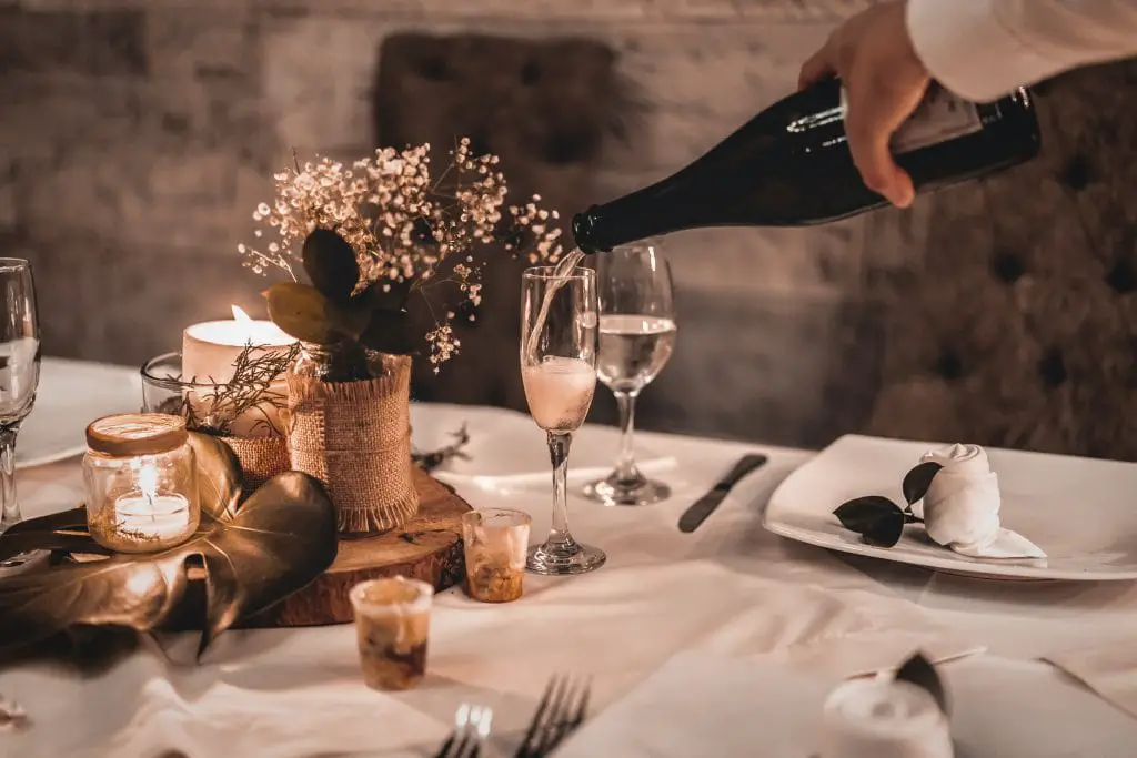 A server pours some champagne into a flute sitting on a table with flowers, candles and plates